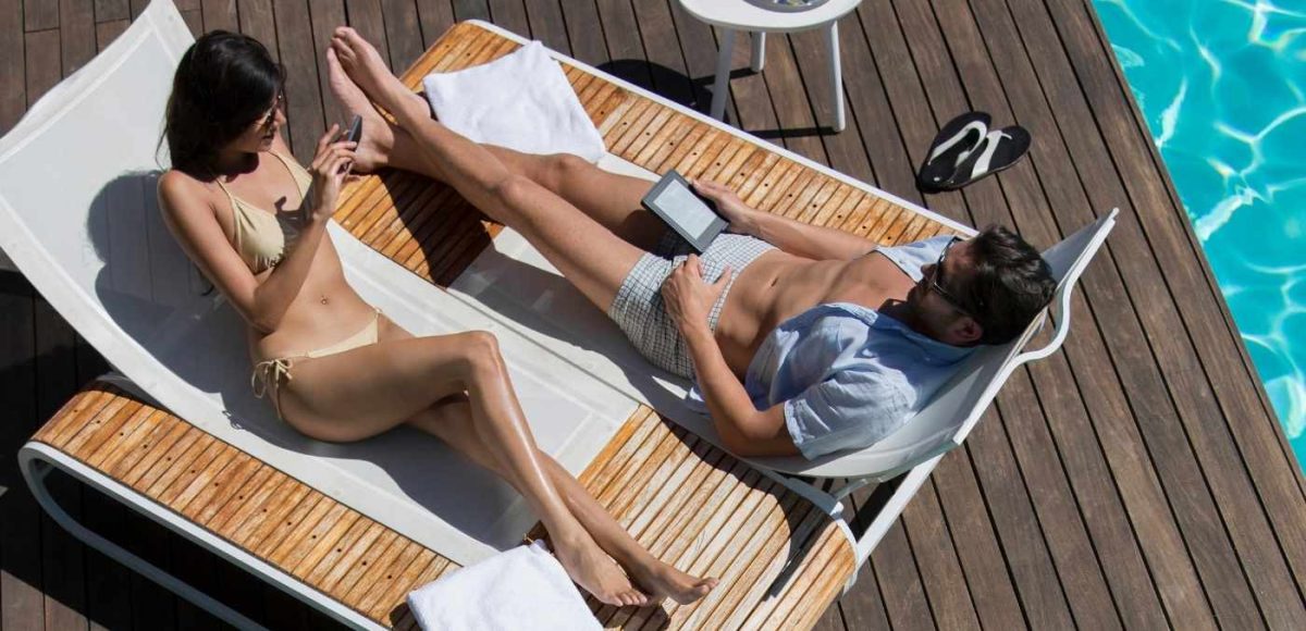 two people on sun loungers with travel accessories in hand